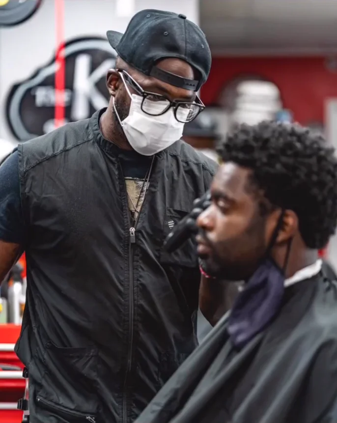 A barber at The Kut Shoppe actively cutting a client’s hair